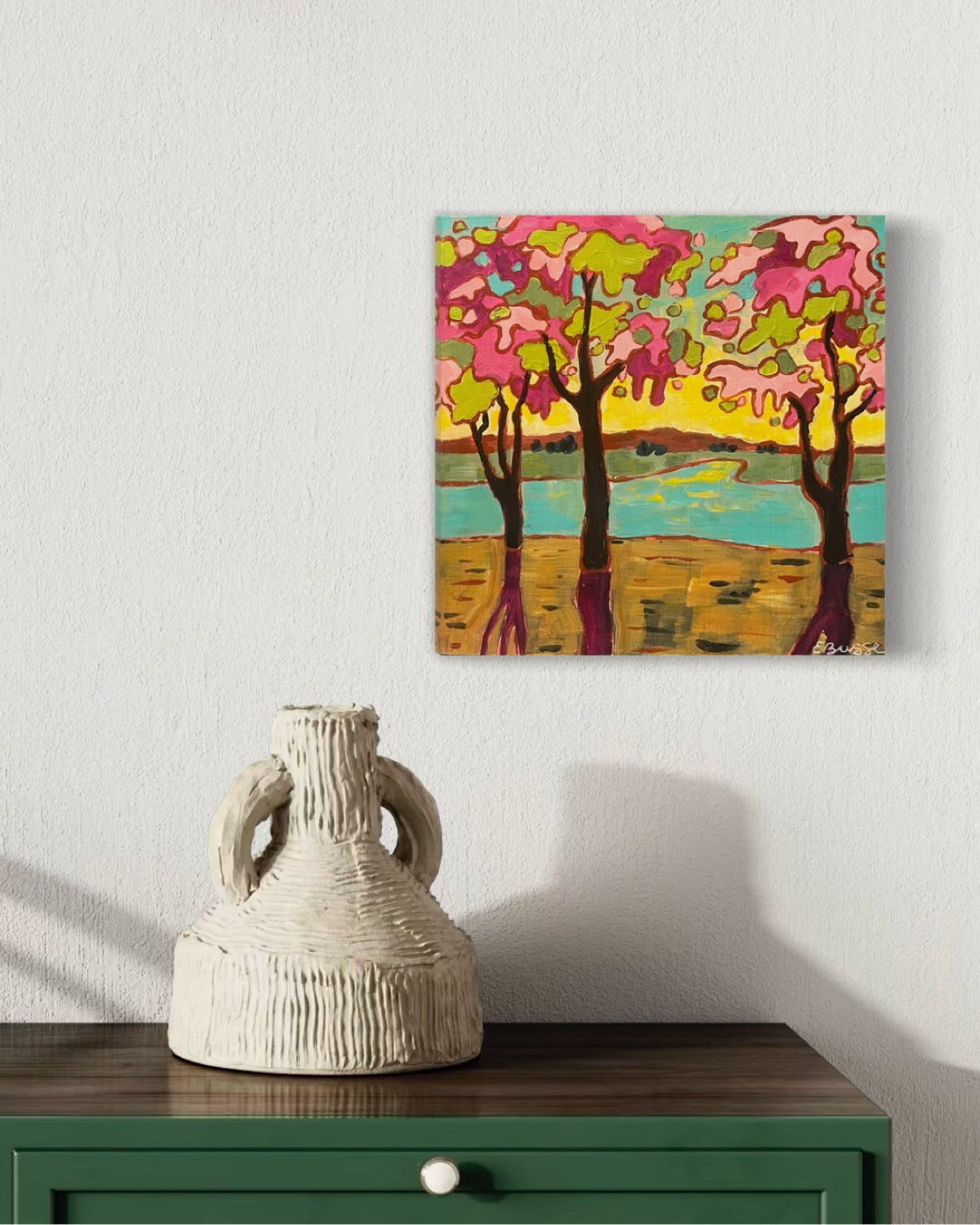 spring trees with pink and limegreen foliage next to a lake at sunset, acrylic painting by asheville artist erika busse. hanging in a room