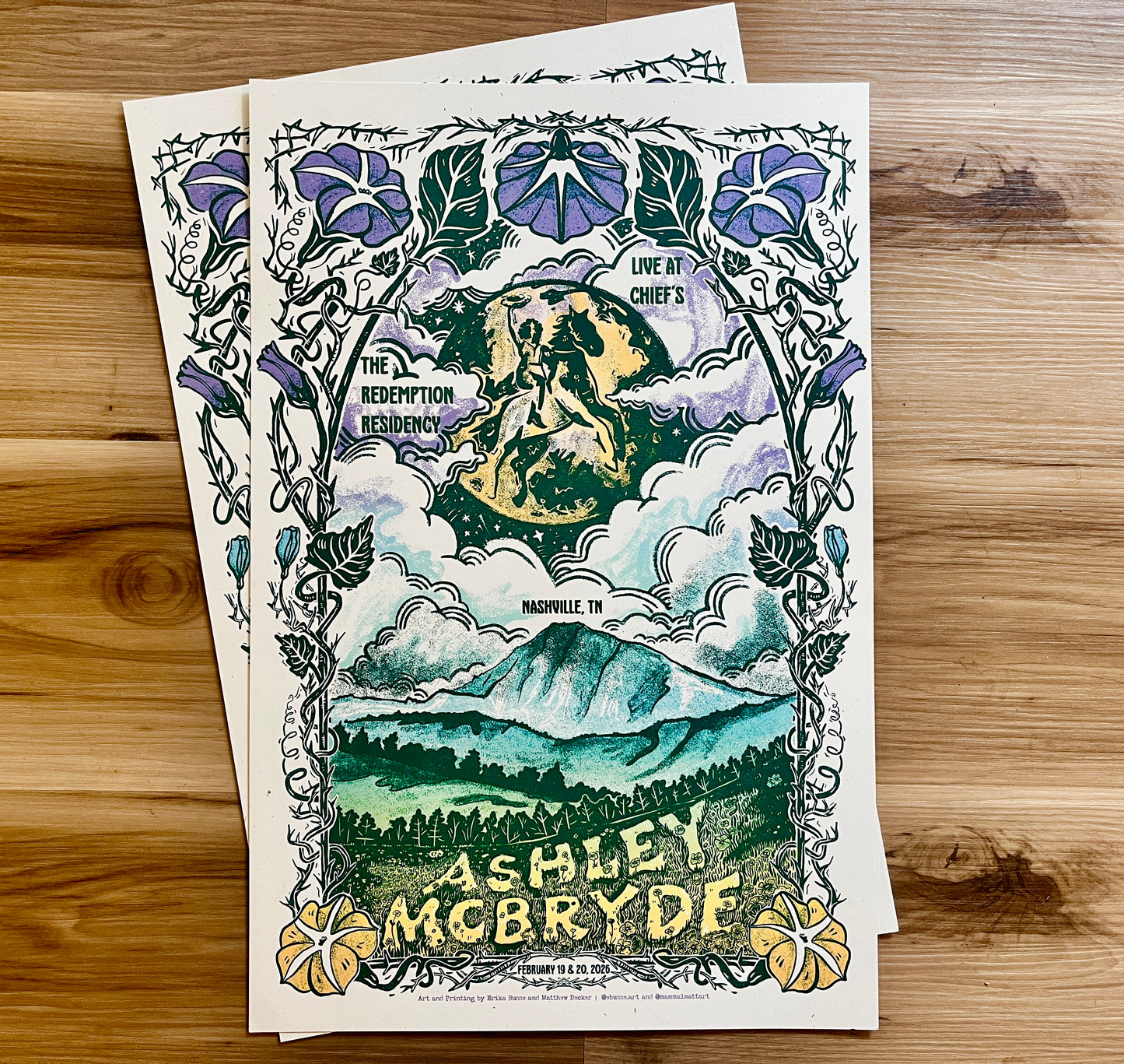 Two concert posters for Ashley McBryde on a wooden surface