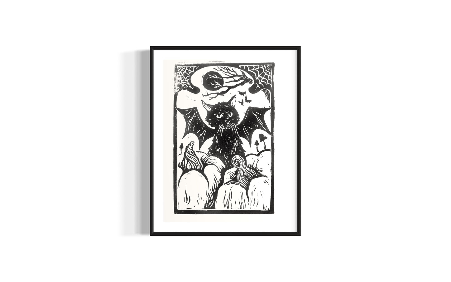 linocut print of a black cat with bat wings surrounded by pumpkins, by asheville artist erika busse in a frame