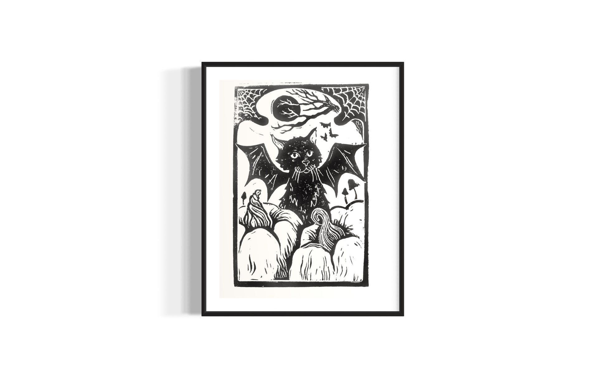 linocut print of a black cat with bat wings surrounded by pumpkins, by asheville artist erika busse in a frame